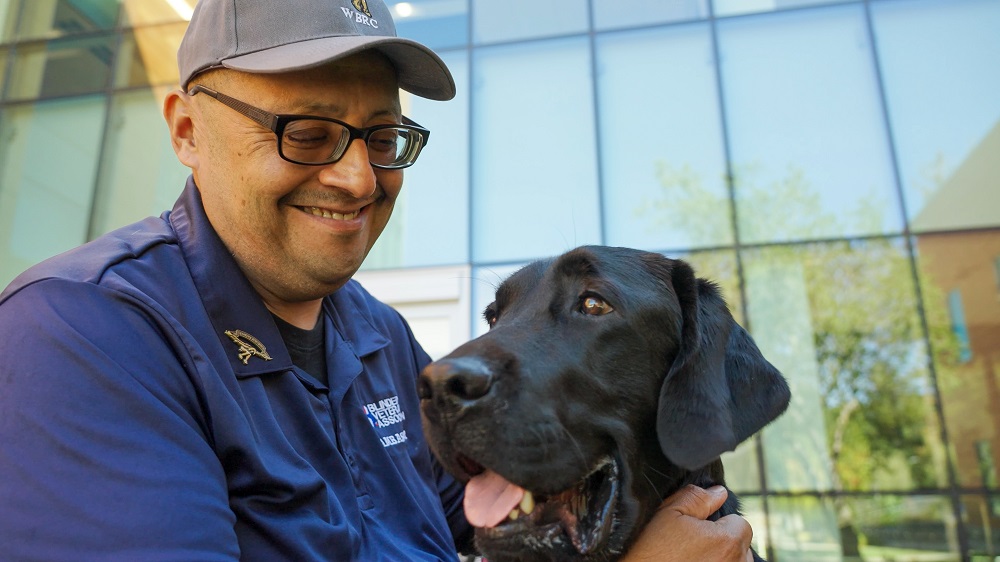Veteran with a smile on his face petting a Black Labrador Retriever service dog