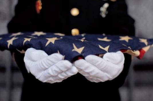 Person in military uniform holding a folded American flag with gold stars.