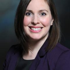 portrait of a smiling person with shoulder length brown hair and a navysuit jacket