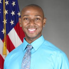 A man in a blue shirt with an American flag in the background