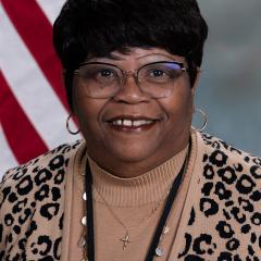 photo of a person with short black hair and glasses, wearing an animal print sweater