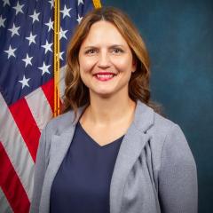 Dr. Sarah Barron smiling while sitting in front of the US Flag