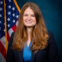 Dr. Auster smiling in front of the US flag and a blue background