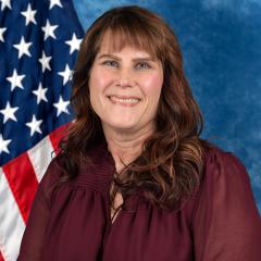 Michelle Wilcox studio portrait. She poses in front of the American flag and a blue background. 