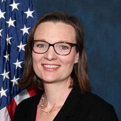 Woman with brown hair in front of flag