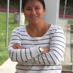 Woman with tan skin, and black hair, with her arms folded and wearing a white top with thin black stripes. 