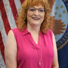 Staff headshot of red headed woman in front of American and Department of V.A. flag.