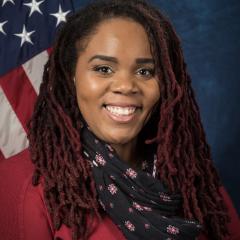 Jasmine Battle seated in front of the American flag wearing a red top and patterned scarf.