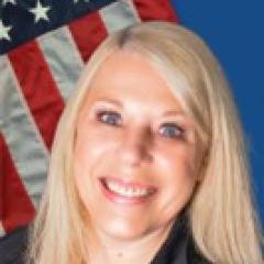 A staff portrait of a smiling woman with blonde hair and an American flag in the background.