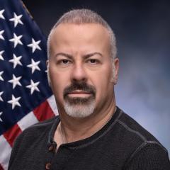 Ali Fout in front of an American Flag and a grey background