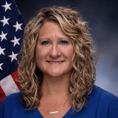 Kim Ziel in front of a flag and a grey background