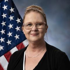 Renea Nichols in front of a flag and a grey background