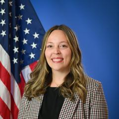 A woman posed in front of an American flag and blue background.