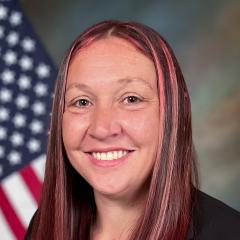 person with brown hair and pink highlights sitting in front of flag