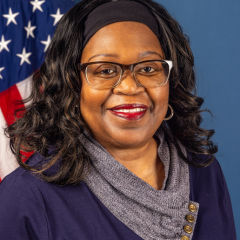 Black woman with black hair in a headband and glasses, smiling