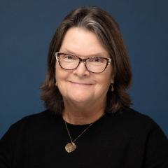 Photograph of a smiling woman with short brown hair wearing glasses and a black shirt.