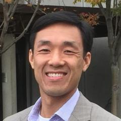 Smiling Asian man in gray suit and blue shirt.