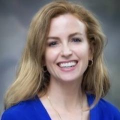 Portrait of a woman with blonde hair, wearing a blue shirt and smiling.