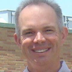 Portrait of a smiling man with gray hair and a blue shirt.
