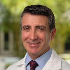 Man in white lab coat and red tie smiling for the camera.