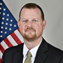 Man in a suit and tie standing in front of an American flag.