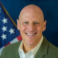 Bald man smiling with American flag in the background.