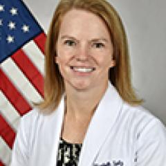 Woman in white lab coat with an American flag in the background.