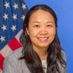 Woman with long black hair smiling in front of an American flag.