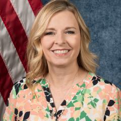 Blonde woman in a floral shirt smiling in front of a US flag.