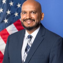 Man in suit and tie smiling in front of American flag.