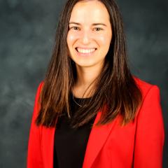 Woman in red blazer and black shirt smiling against a gray background.