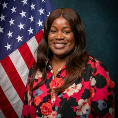 Woman in floral shirt smiling in front of American flag.