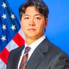 Man in suit and tie stands in front of the American flag.