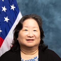 A smiling Asian woman in front of an American flag.