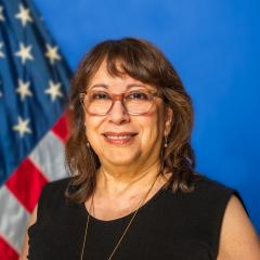 Woman smiling with American flag in the background.
