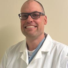 Bald man in white lab coat and glasses smiling.