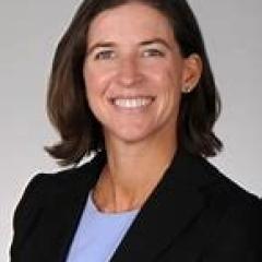 Woman in black blazer and blue shirt smiling at the camera.
