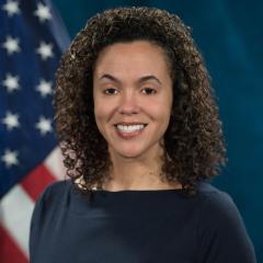 Woman with curly hair smiling in front of an American flag.