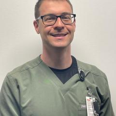 Smiling man in green scrubs with stethoscope around his neck.