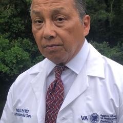 Headshot of an older man in a white lab coat and red necktie.