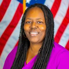 Portrait of smiling African American woman in purple blouse with American flag in background.