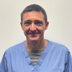 Portrait of a smiling man in blue scrubs against a plain white background.