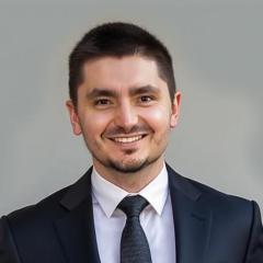 A smiling man in a black suit and tie poses for a photo.