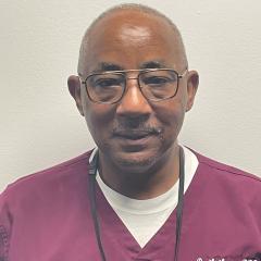 Photo of a man in red scrubs and glasses smiling.