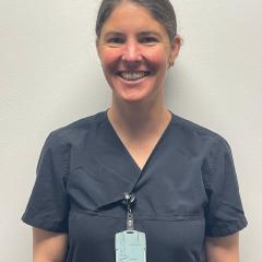 Smiling woman in dark blue scrubs with a light blue ID badge.