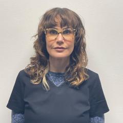 Woman with curly hair wearing glasses and a dark blue shirt.