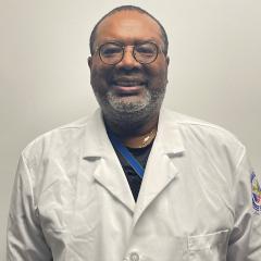 Man in white lab coat and glasses smiles against plain white background.