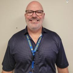 Smiling bald man with glasses and a blue lanyard.