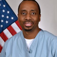 Man in blue scrubs smiling in front of an American flag.