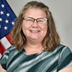 Woman with glasses smiling with US flag in background.